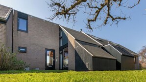Een modern gebouw met een schuin dak, een bakstenen gevel en een gazon met margrietjes.