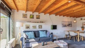 Een moderne woonkamer met een houten plafond, een grijze bank, een houten salontafel en een eethoek met een witte tafel en stoelen.