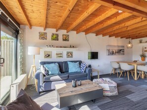 A modern living room with a wooden ceiling, a grey sofa, a wooden coffee table, and a dining area with a white table and chairs. - Zeenatuur by Interhome (Burgh-Haamstede)