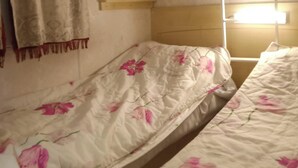 A room with two single beds, a wooden headboard, a window with a white blind, and a wall-mounted shelf. - Mobi The Man. (Couret)