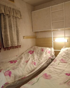 A room with two single beds, a window with a curtain, a wall-mounted shelf, and a ladder. - Mobi The Man. (Couret)