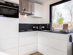 Een moderne keuken met witte kasten, een zwart aanrecht, een inbouwoven en een raam met uitzicht op bomen.