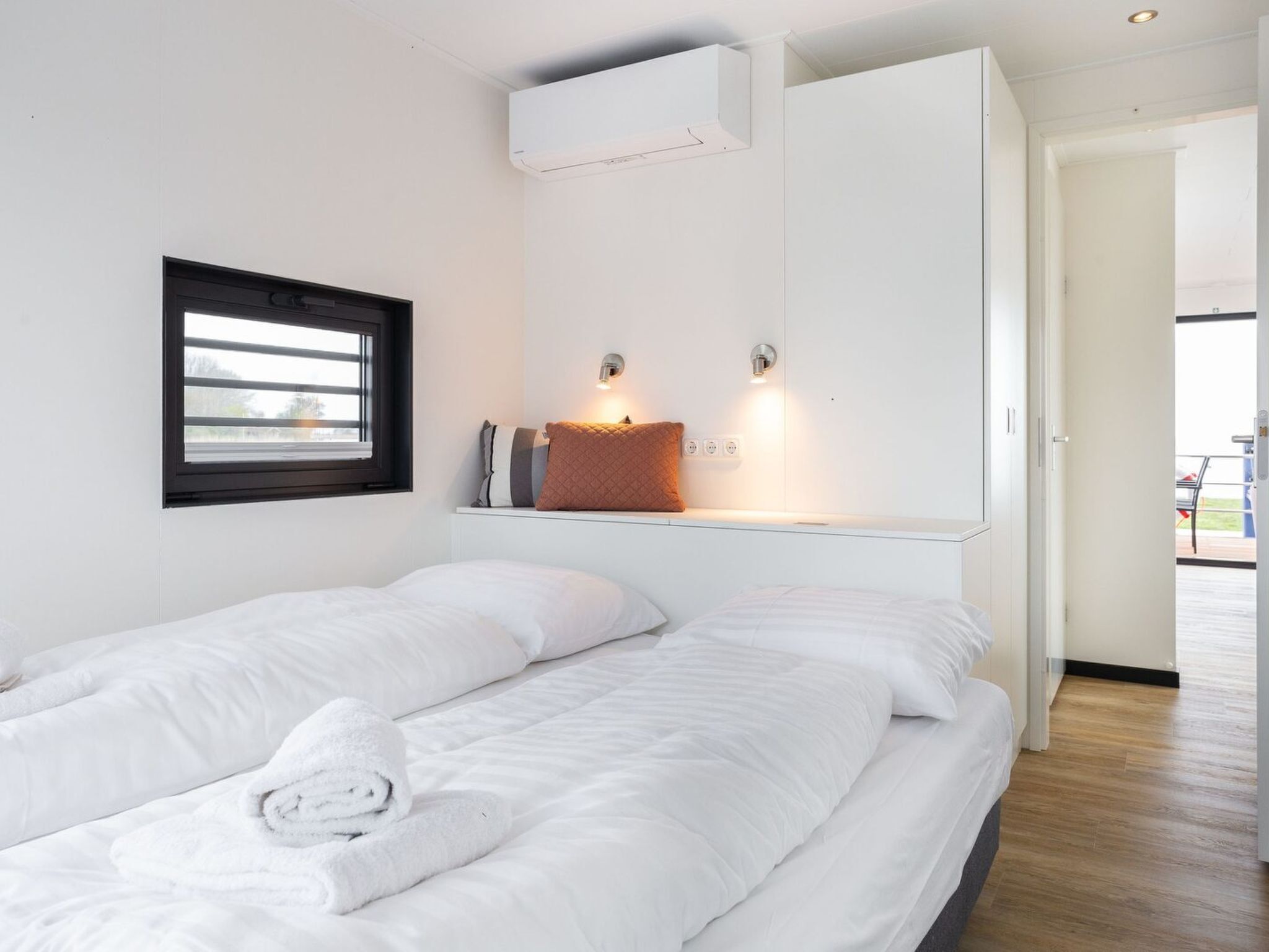 A modern hotel room with two beds, a window, an air conditioning unit, and a view of the outside.