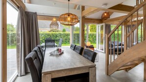 Un vaste espace dédié à la salle à manger, avec une table et des chaises en bois, de grandes fenêtres et un escalier.