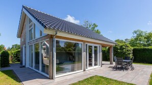 Une maison moderne dotée d’une grande extension en verre, d’un patio avec mobilier d’extérieur et d’une pelouse bien entretenue.