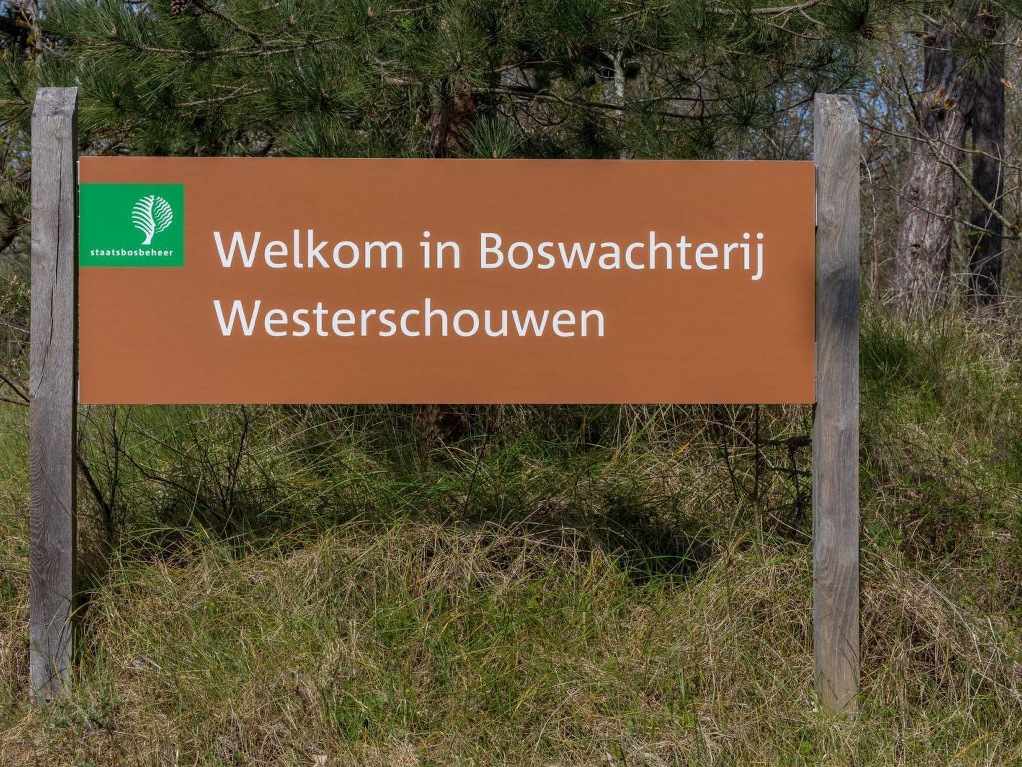 Welkomstbord met tekst in het Nederlands, omgeven door bomen en gras.