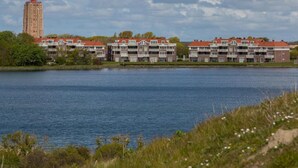 Ein Anwesen am Wasser mit einem markanten Turm, mehrstöckigen Gebäuden mit Balkonen und einer Wasserfläche.