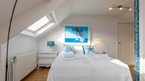 Ein Schlafzimmer mit Dachfenster, einem Bett mit weißer Bettwäsche, einem Delfinbild, einem Seesternkissen und einer blauen Seisterndekoration.