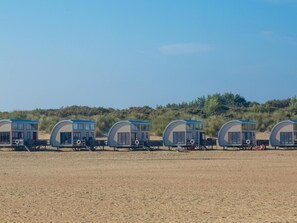Eine Reihe von Strandhütten mit Sandstrand und Dünen im Hintergrund.