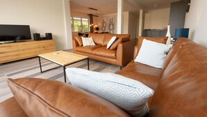 Una sala de estar moderna con un sofá de cuero, una mesa de centro y un televisor sobre un mueble de madera.