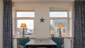 Ein Zimmer mit Tisch und zwei Stühlen, einer Stern-Dekoration an der Wand und Fenstern mit Vorhängen.