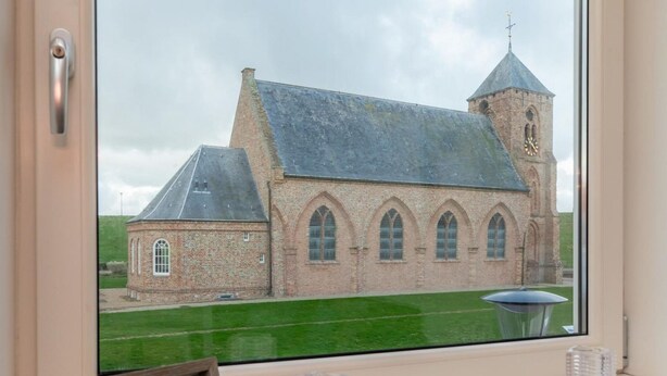 Ein Fenster mit Blick auf eine Backsteinkirche mit einem Glockenturm und ein kleines Gebäude zur Linken.