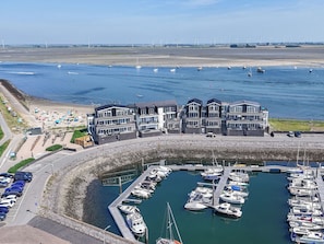 A marina with boats docked, a beach with people, and a building with multiple floors. - Vento Marin by Interhome (Sint-Annaland)