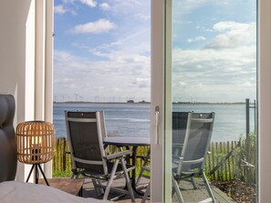 Ein Balkon mit zwei Stühlen und einem Tisch, mit Blick auf ein Gewässer, in der Ferne Windkraftanlagen.
