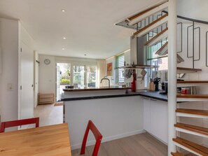 Een moderne keuken met een centraal eiland, houten vloeren en een trap met een leuning.