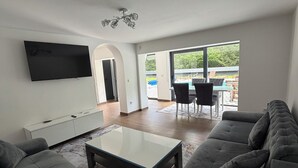 Una sala de estar moderna con un televisor de pantalla plana, un sofá, una mesa de centro y un comedor con sillas.