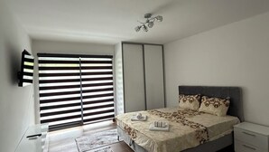 Un dormitorio con cama, mesitas de noche, televisor y ventana con persianas.