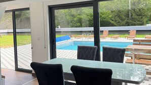 Una habitación moderna con una mesa y sillas de vidrio, un ventanal con vistas a una piscina y zona de estar al aire libre.