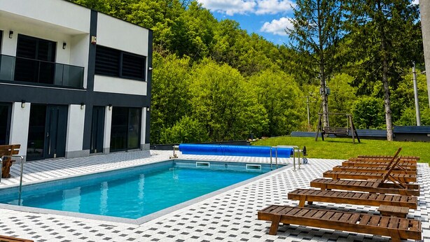 Un edificio moderno con piscina, sillones de madera y un diseño de baldosas tipo espiga.
