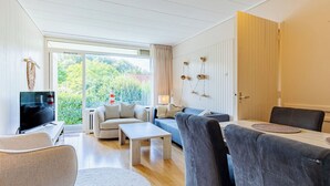 Una sala de estar moderna con televisor, sofás, una mesa de centro y un comedor con sillas.