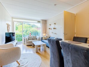Een moderne woonkamer met een televisie, banken, een salontafel en een eethoek met stoelen.