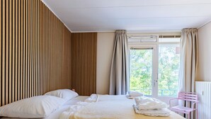 Una habitación de hotel con cama, ventana, radiador y una silla rosa.