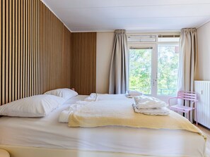 Een hotelkamer met een bed, een raam, een radiator en een roze stoel.