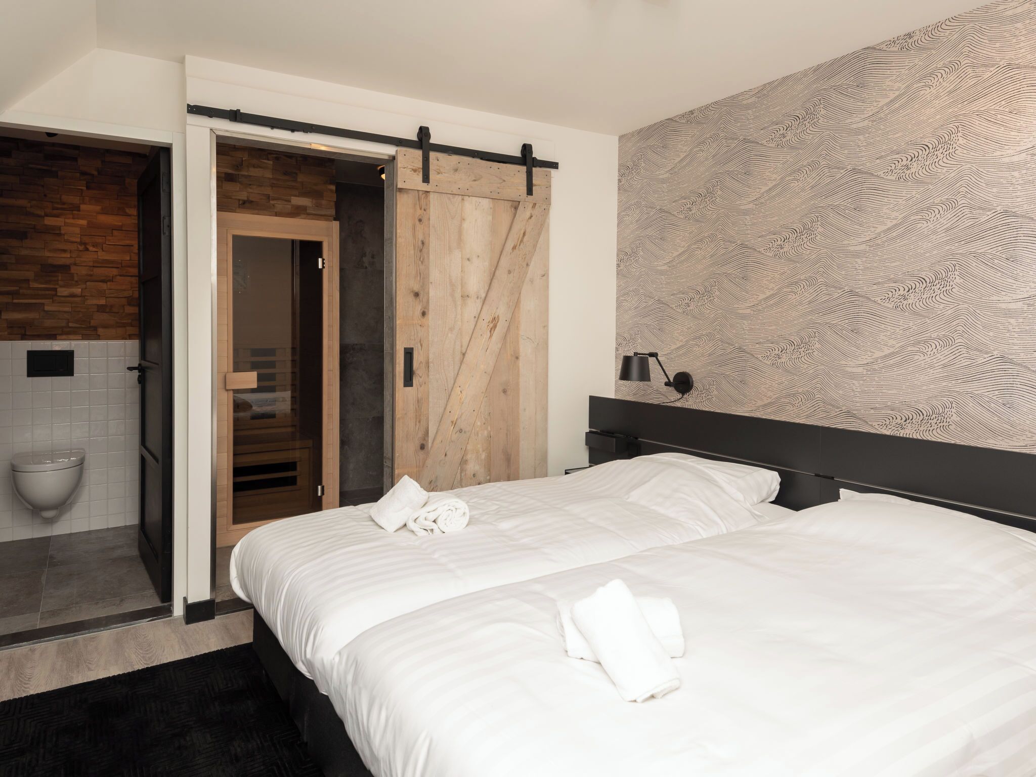 A modern bedroom with a wooden wardrobe, a black headboard, and a patterned wall.