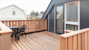 A wooden deck with a table and chairs, a sliding glass door, and a white building in the background. - Bomont ZandStrand by Interhome (Renesse)