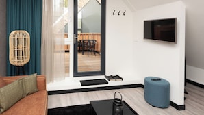 A modern living room with a sofa, a TV, a wicker floor lamp, a blue ottoman, and a sliding glass door leading to a balcony. - Bomont ZandStrand by Interhome (Renesse)