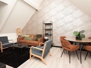 A modern loft-style living space with a high ceiling, a dining area, and a built-in bookshelf. - Bomont ZeeGolf by Interhome (Renesse)