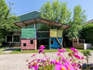 Een meerlaags houten constructie met een groen dak, een blauw gedeelte beneden en een rood gedeelte boven, omringd door groen.