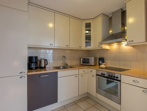 Een moderne keuken met witte kastjes, een roestvrijstalen afzuigkap, een magnetron en een koffiezetapparaat.