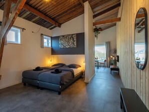 Ein Schlafzimmer mit zwei Betten, Holzboden, einem großen Spiegel und Blick ins Freie.