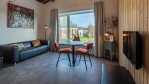 Ein modernes Wohnzimmer mit einer schwarzen Couch, zwei roten Sesseln, einem runden Tisch und einem Fernseher an der Wand.