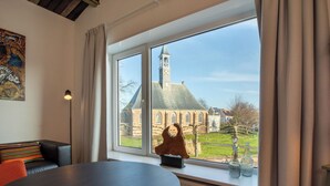 Ein Zimmer mit einem runden Tisch, einer Couch, einem Fenster mit Blick auf ein Gebäude mit einem Uhrturm und einer Skulptur auf der Fensterbank.