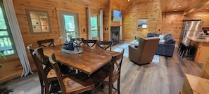 A wooden cabin interior with a dining area, a sofa, and a kitchen. - Bear Hug Hideaway: Secluded 2 King Cabin, Epic Arcade +Hot Tub, 4 min to Parkway (Sevierville)