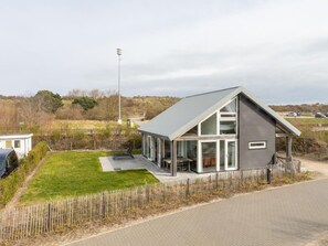 Ein modernes Haus mit Satteldach, großen Glasfenstern und einem gepflasterten Einfahrt.