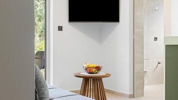 Ein modernes Zimmer mit einem an der Wand befestigten Flachbildfernseher, einem runden Holztisch mit Obstschale und einem grauen Sofa.