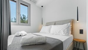 Habitación de hotel moderna con una cama grande, una mesita de noche pequeña, una ventana con cortinas y una lámpara fijada a la pared.