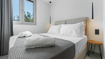 A modern hotel room with a large bed, a small bedside table, a window with curtains, and a wall-mounted light fixture.