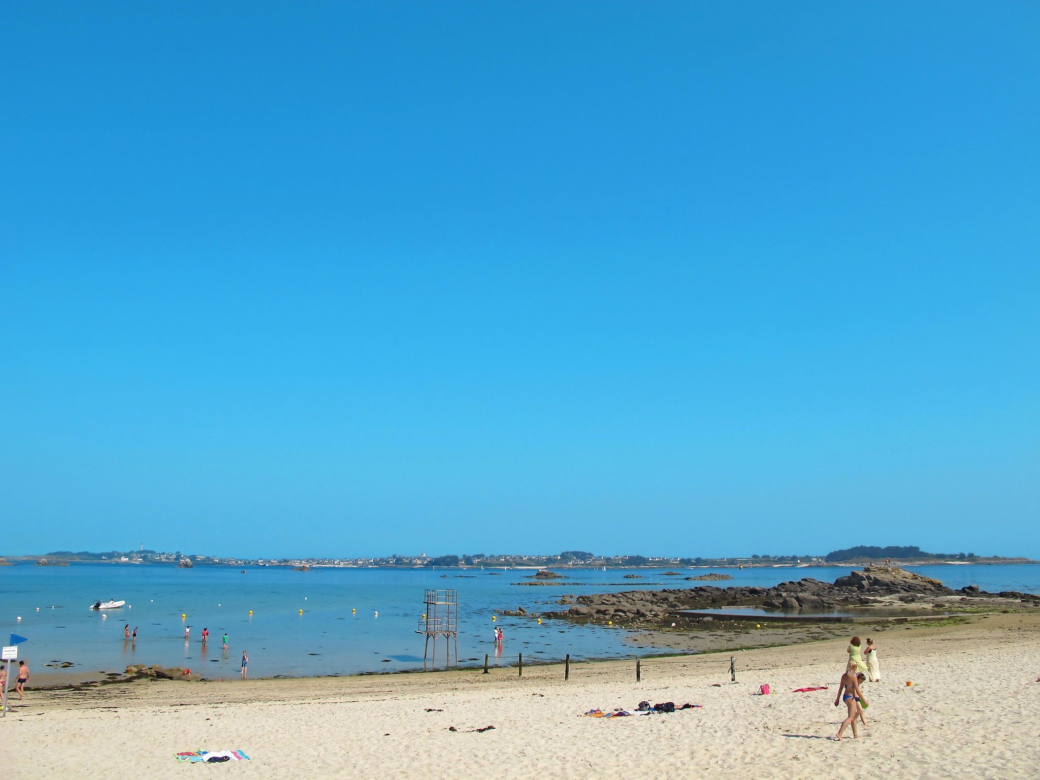 A beach with clear skies, calm water, and a lifeguard tower.