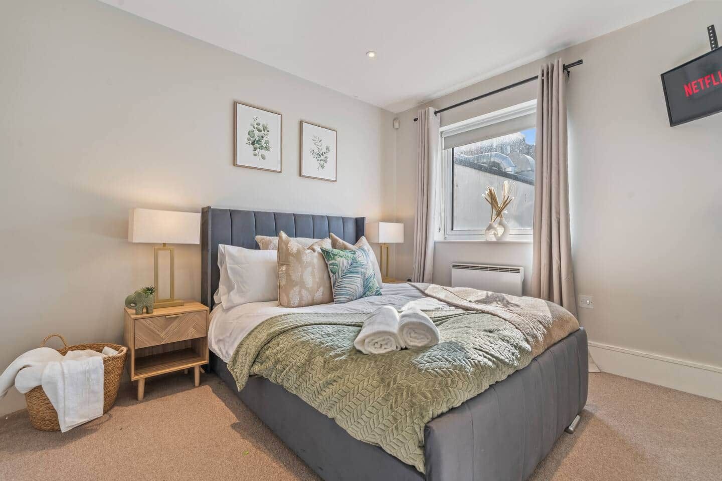 A bedroom with a bed, bedside tables, a window with curtains, and a wall-mounted TV.