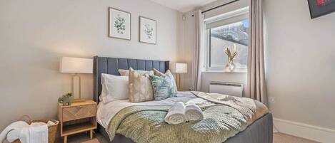 A bedroom with a bed, bedside tables, a window with curtains, and a wall-mounted TV.
