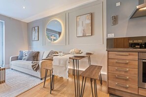 A modern living room with a sofa, a dining table with chairs, a kitchen area with cabinets, and a large mirror on the wall. - Central London NEW luxury apartment by kings cross (London)