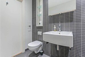 Et badeværelse med et hvidt toilet, en hvid vask og et spejl over vasken.