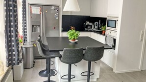 Een moderne keuken met een centraal eiland, barstoelen, een koelkast en een magnetron.