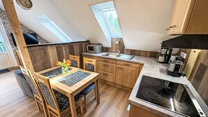 A compact kitchen with wooden cabinets, a dining table with chairs, a built-in microwave, and a coffee maker. - Apartment Fecht by Interhome (Marienhafe)
