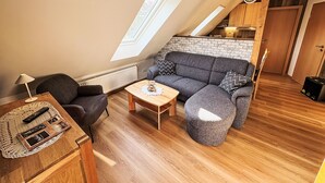 A loft-style living space with a sloped ceiling, a built-in kitchen, and a cozy seating area with a sofa and ottoman. - Apartment Fecht by Interhome (Marienhafe)