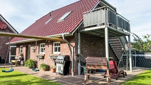 A house with a red-tiled roof, a covered patio area, a brick exterior, and a wooden deck. - Apartment Fecht by Interhome (Marienhafe)